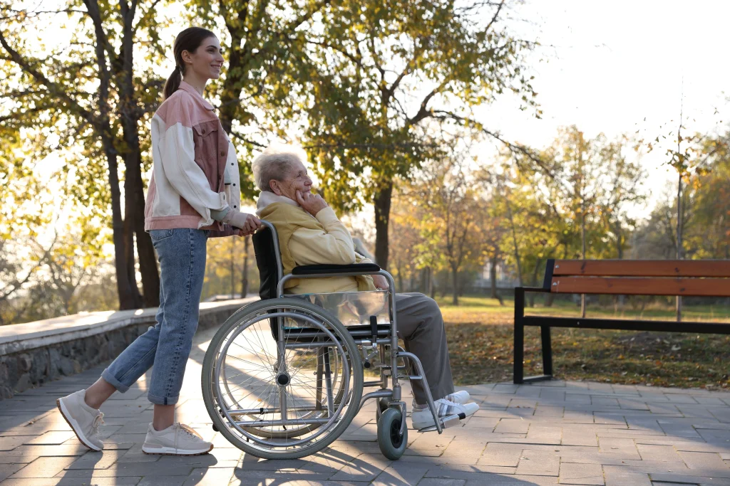 Opiekunka towarzyszy seniorowi z chodzikiem podczas spaceru w parku
