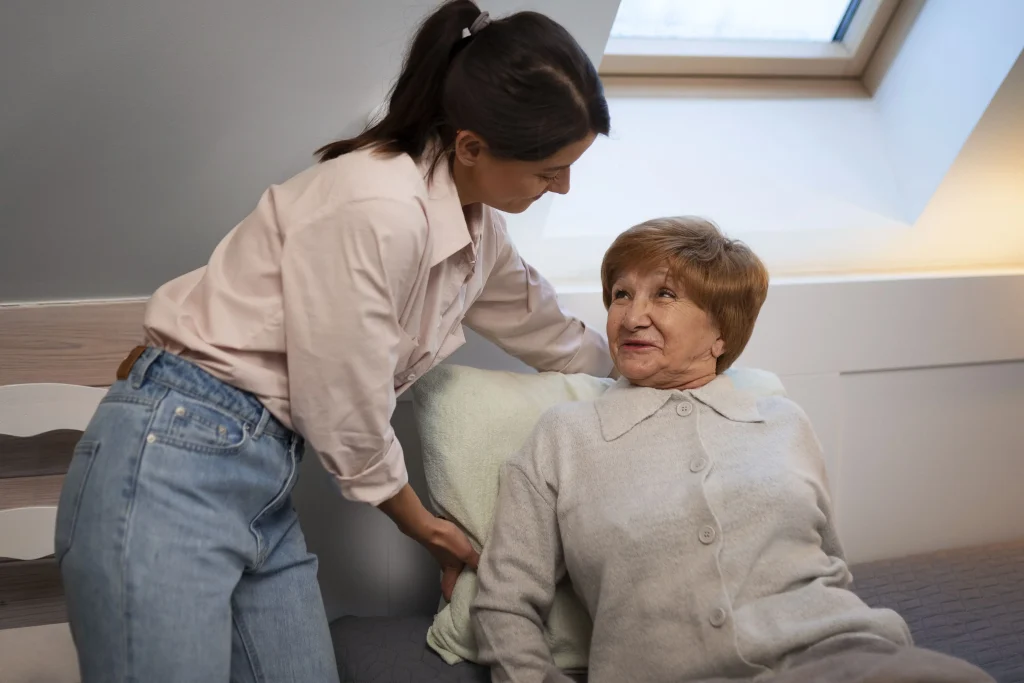 Opiekunka pomaga seniorce usiąść na brzegu łóżka rano